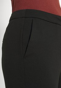 Mustat housut, joissa on sileä ja joustava kangas; sivutaskut ja räätälöity istuvuus. Vyötärönauha on joustava ja istuu luonnollisesti vyötärölle.