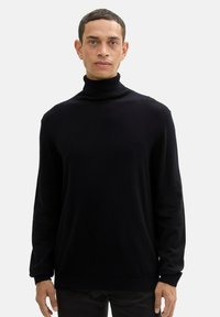 Pull en col roulé noir avec une texture côtelée, des manches longues et une coupe décontractée. Le tissu semble doux et léger. Aucun motif ou accent visible.