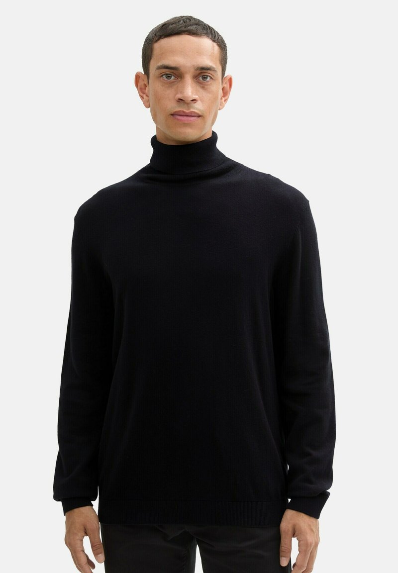 Pull en col roulé noir avec une texture côtelée, des manches longues et une coupe décontractée. Le tissu semble doux et léger. Aucun motif ou accent visible.
