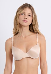 Soutien-gorge sans fil beige fabriqué en tissu doux. Comprend des bonnets moulés, des bretelles réglables fines et un design sans coutures pour plus de confort.