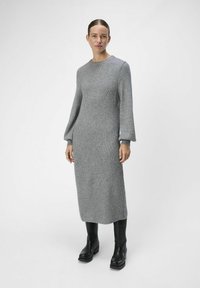Abito grigio a coste con maniche lunghe a puffo e scollatura rotonda. Indossato con stivali neri con tacco spesso. Design minimalista.