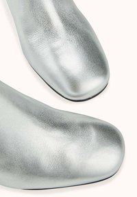 Bottines argentées en cuir texturé, avec un bout arrondi et une finition lisse. Semelles noires au design minimaliste.