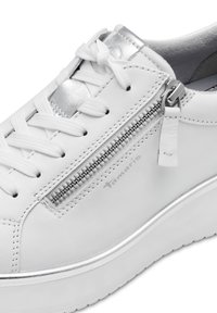 Sneaker in pelle bianca con accenti metallici argentati, caratterizzato da dettagli con zip, lacci e una suola texturizzata bianca. Marchio visibile sul lato.