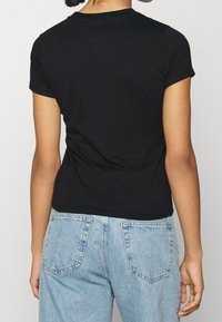 Svart kortärmad t-shirt i bomull, figurformad design med rund fyrkant och något böjt nederkant, matchad med ljusblå denimjeans.