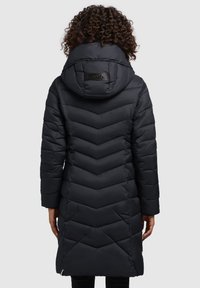 Manteau matelassé noir avec un design à chevrons, une grande capuche et un accent logo dans le dos. Manches longues et coupe mi-genoux. Texture lisse.