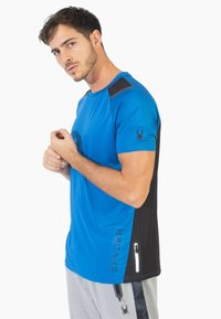Camiseta deportiva azul con detalles en negro, con mangas cortas, cuello redondo y un bolsillo con cremallera lateral. Logo de la marca en la manga.