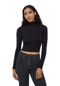 Top nero a coste, corto, con collo alto e chiusura con mezza zip; abbinato a jeans scuri a vita alta con tasche anteriori.