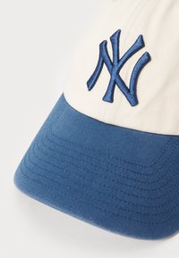 Baze bal kapica u krem i plavoj boji, s plavim vezivom "NY" logom. Teksturisani plavi vizir s rebrastim uzorkom. Izrađena od pamuk mješavine.