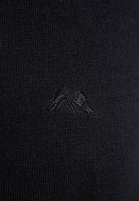 Dunkel gestrickter Stoff mit einem subtilen gestickten Design von zwei gekreuzten Flaggen in schwarzem Faden in der Mitte.