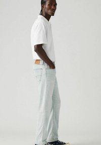 Light blue denim jeans with a straight-leg cut, featuring a brown leather patch at the back, paired with a fitted white polo shirt.