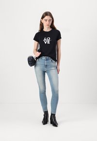 Fekete pamut póló "LOVE" grafikával, világoskék skinny farmerrel és fekete sarka ankle csizmával párosítva. A modell egy kompakt fekete táskát tart.