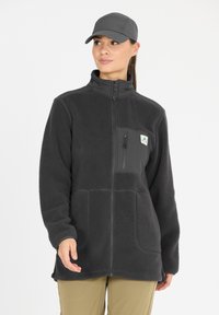 Musta fleece-takki, jossa on korkea kaulus, vetoketjukiinnitys ja kaksi suurta taskua; siinä on pieni logo rinnassa ja teksturoitu kangas.
