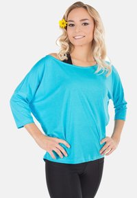 Light blue, loose-fitting top with a wide neckline and three-quarter sleeves, paired with black leggings. Smooth textile, casual design.
