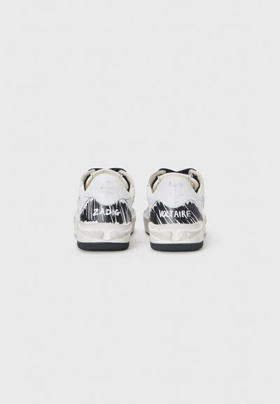White sneakers with black and white abstract patterns on the heel, featuring a textured sole and contrasting black rubber accents.