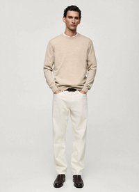 Maglione beige a maglia, pantaloni bianchi e stivali neri. Il maglione presenta un collo rotondo; i pantaloni sono larghi con una superficie liscia.