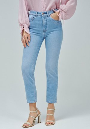 Jeans de tiro alto en azul claro con un ajuste Slim, con bolsillos laterales y un ligero estrechamiento en el tobillo, combinados con tacones de tiras en beige claro.