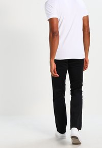 Černé kalhoty s přímo střiženým střihem, vyrobené z lehké látky, ve spojení s bílým tričkem a bílými teniskami. Minimalistický design, bez vzorů.