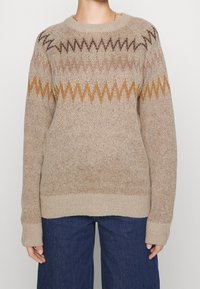 Beżowy sweter dzianinowy z zygzakowym wzorem w brązowym, złotym i rdzawym kolorze, z okrągłym dekoltem i ściągaczem na dole, wykonany z teksturowanej tkaniny.