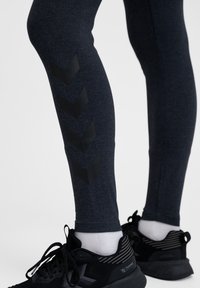 Tekniska leggings i mörkgrått tyg med svarta chevron-detaljer längs vaden. Svarta träningsskor med vita strumpor fulländar looken.