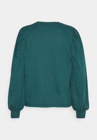 Blusa larga de color verde azulado, hecha de una tela suave, con mangas abullonadas y escote redondo. Textura suave con puños acanalados en los extremos de las mangas.