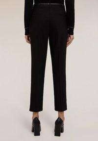 Zwarte tailored broek met een slim fit, voorzien van achterzakken en een gladde textuur. Gecombineerd met zwarte, chunky-heeled schoenen.