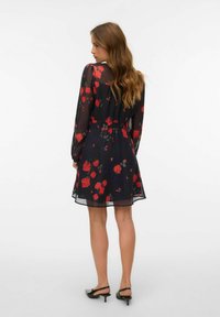 Crna cvjetna haljina s dugim prozirnim rukavima, uzorcima crvenog cvijeća, elastičnim strukom i lepršavom suknjom. Nošena s crnim cipelama na petu.