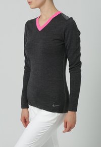 Haut gris à manches longues avec col en V, bordé de passepoil rose autour de l'encolure, coupe près du corps, et petit logo Nike argenté près de l'ourlet. Texture lisse.