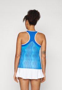 Blå atletisk linne med mönstrad textur, racerback-design och vit kant, ihop med en vit kjol. Slät tygfinish.