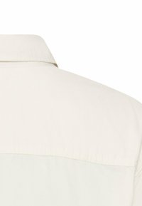 Lichtbeige shirtkraag met een gladde textuur, met een gedeeltelijk zicht op de achterkant en een horizontale naaddetail bij de schouder.