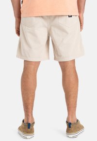 Pantalones cortos de pana color beige claro con dos bolsillos traseros, de largo por encima de la rodilla, corte recto, combinados con unos zapatos de ante marrones y una blusa melocotón.