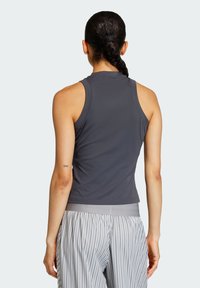 Majica bez rukava, tamno siva atletska majica s glatkom teksturom i prilagođenim dizajnom. Nosimo je s hlačama svijetlo sive boje sa prugama i rastezljivim pojasom.