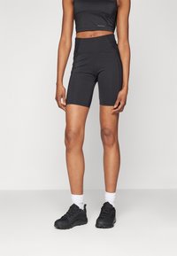 Svarta högmidjade cykelshorts med en slät, elastisk yta och söms detaljer. Kombinerade med svarta sneakers och vita ankelsockor.