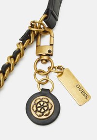 Goudkleurige metalen ketting en hardware, met een zwart leren label met een bloemenontwerp en een gouden "GUESS" label.