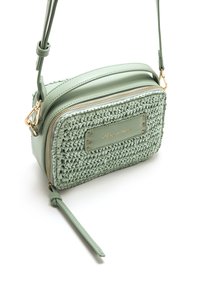 Bolso cruzado verde con textura y detalles tejidos, herrajes en tono dorado y cierre de cremallera. Cuenta con una correa delgada ajustable.