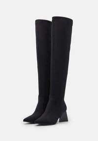 Zwarte kniehoge laarzen van rekbaar materiaal. Puntige neus, blokhak en een gladde textuur met een ritsdetail aan de achterkant.