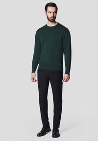 Ciemnozielony sweter z okrągłym dekoltem, wykonany z teksturowanej dzianiny, zestawiony z dopasowanymi czarnymi spodniami i czarnymi butami typu lace-up.