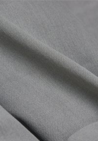 Gros plan sur un tissu gris clair lisse avec une texture visible de fine armure diagonale et de légers plis.