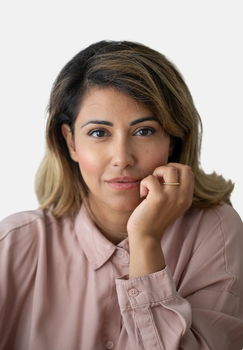 Nahaufnahme einer Person mit schulterlangen, welligen Haaren, die ein hellrosa, knöpfbares Hemd trägt. Sie haben einen goldenen Ring an ihrer rechten Hand.