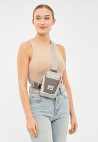 Borsa a tracolla grigia chiara realizzata in materiale resistente. Presenta una forma rettangolare, una tracolla regolabile e una tasca frontale con etichetta.