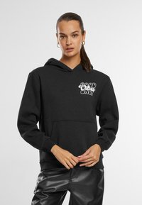 Black hoodie made of cotton blend, featuring a front pocket and a graphic design reading "GOOD VIBES ONLY" in white. Machine washable.