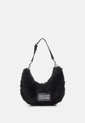 Sac d'épaule en fausse fourrure noire avec une bandoulière réglable en cuir noir et un patch rectangulaire portant l'inscription "Versace Jeans Couture" à l'avant.