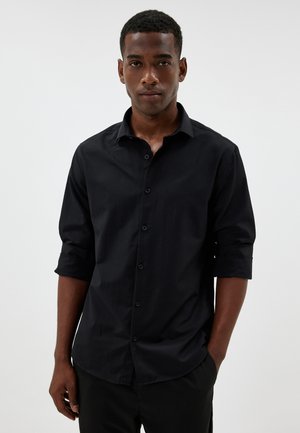 Black button-up shirt with a plain texture, rolled sleeves, and a classic collar. Made from fabric that appears smooth and lightweight.