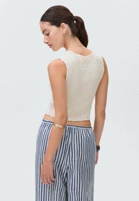 Textured cream crop top with scalloped edges, paired with blue and white striped wide-leg pants. The outfit features minimal accessories.
