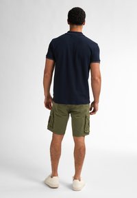 Námořnická polo košile s krátkým rukávem, khaki cargo šortky s bočními kapsami a bílé tenisky na neutrálním pozadí.