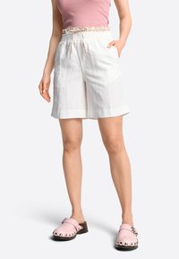 Witte linnen shorts met een smockband met patroon en zakken. Gecombineerd met roze klompen met decoratieve studs.