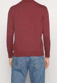 Bordeauxfarbener Strickpullover mit langen Ärmeln, tailliertem Saum und geripptem Kragen. Kombination mit lässig geschnittenen hellblauen Jeans.
