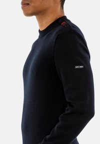 Maglione navy a maglia con texture a coste, collo a giro e dettagli in bottoni sulle spalle. Presenta un'etichetta con logo sulla manica.