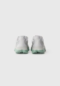 Une paire de chaussures de sport grises et vert clair vues de l'arrière sur un fond blanc, avec des semelles texturées et des cols rembourrés.