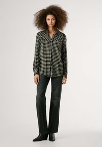 Camicia a quadri bianca e nera con maniche lunghe, abbinata a pantaloni in denim scuro e stivaletti neri con texture.