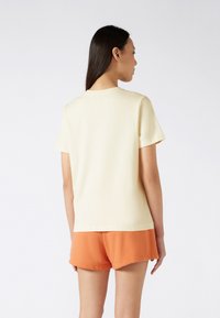 T-shirt en coton crème à manches courtes, encolure ronde et coupe décontractée, associée à un short orange. Design simple, texture lisse.